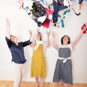 Three women joyfully toss colourful fabric scraps into the air, celebrating creativity and reuse in a bright indoor space.